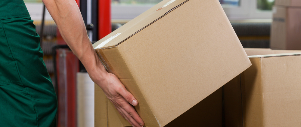 Hands of warehouse worker lifting box, horizontal