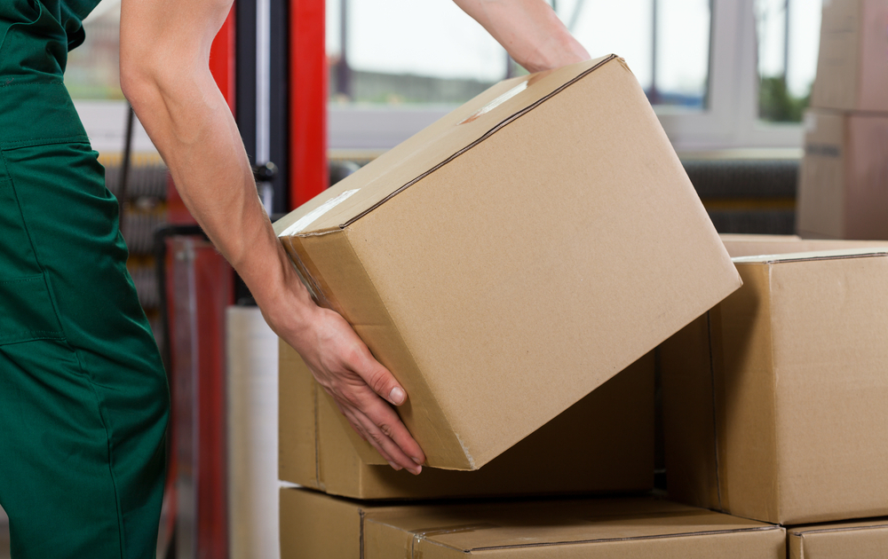 Hands of warehouse worker lifting box, horizontal