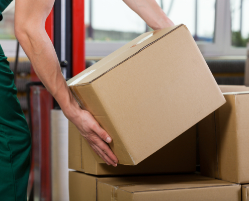 Hands of warehouse worker lifting box, horizontal