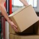 Hands of warehouse worker lifting box, horizontal